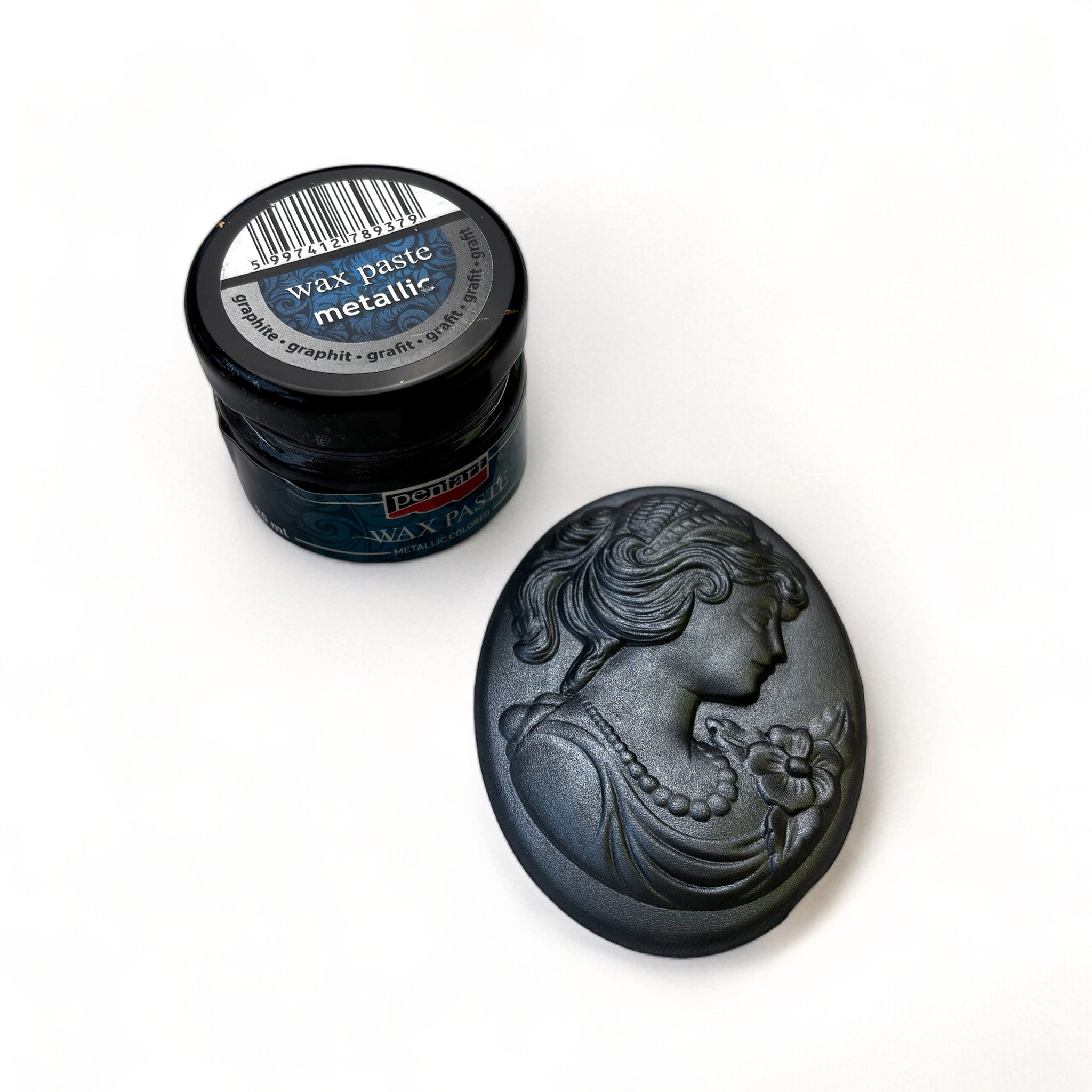 A jar of Pentart's Graphite Metallic Wax Paste and a silicone mold casting of a cameo pendant finished in the wax are against a white background.