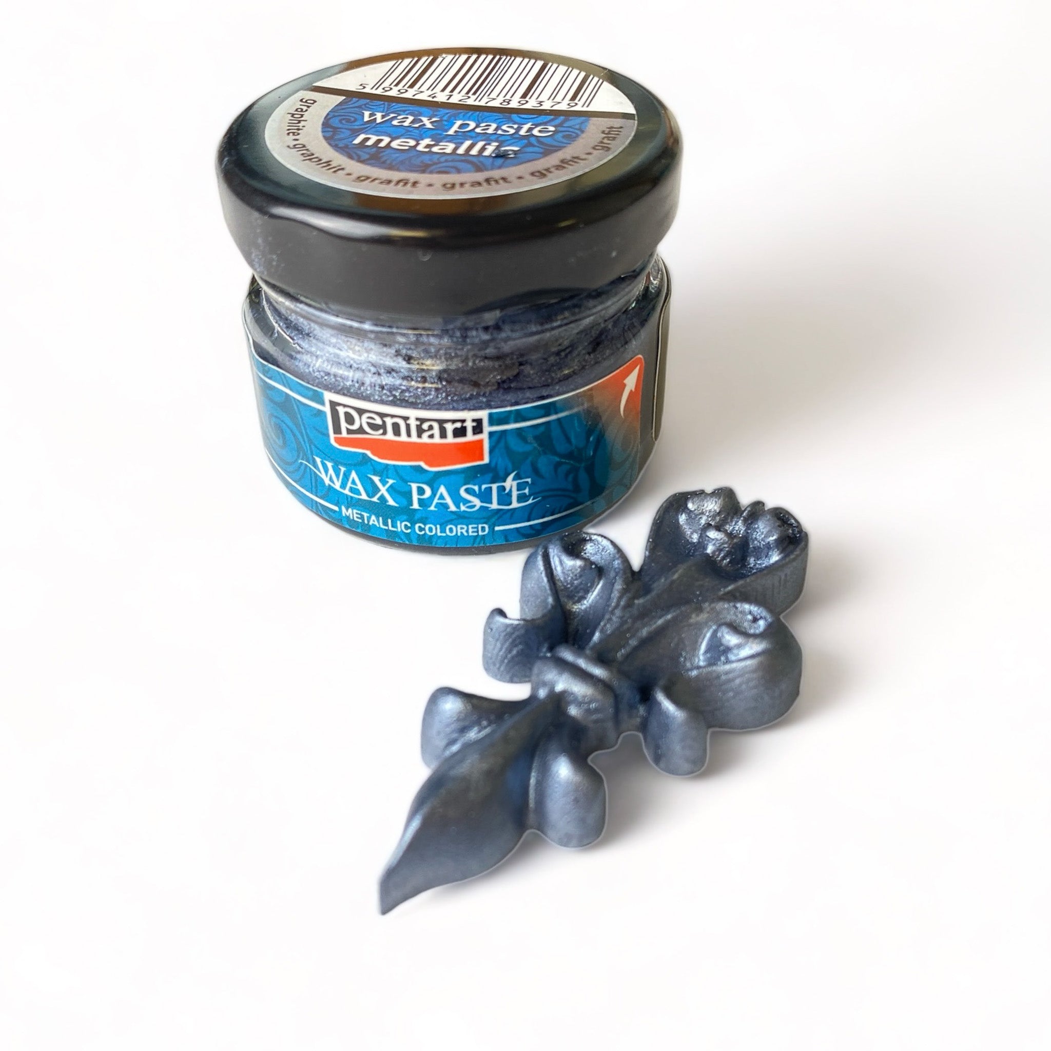 A 0.68 ounce jar of metallic graphite wax paste by Pentart is against a white background. A small silicone casting of an ornate small decor piece is shown with the wax on it.