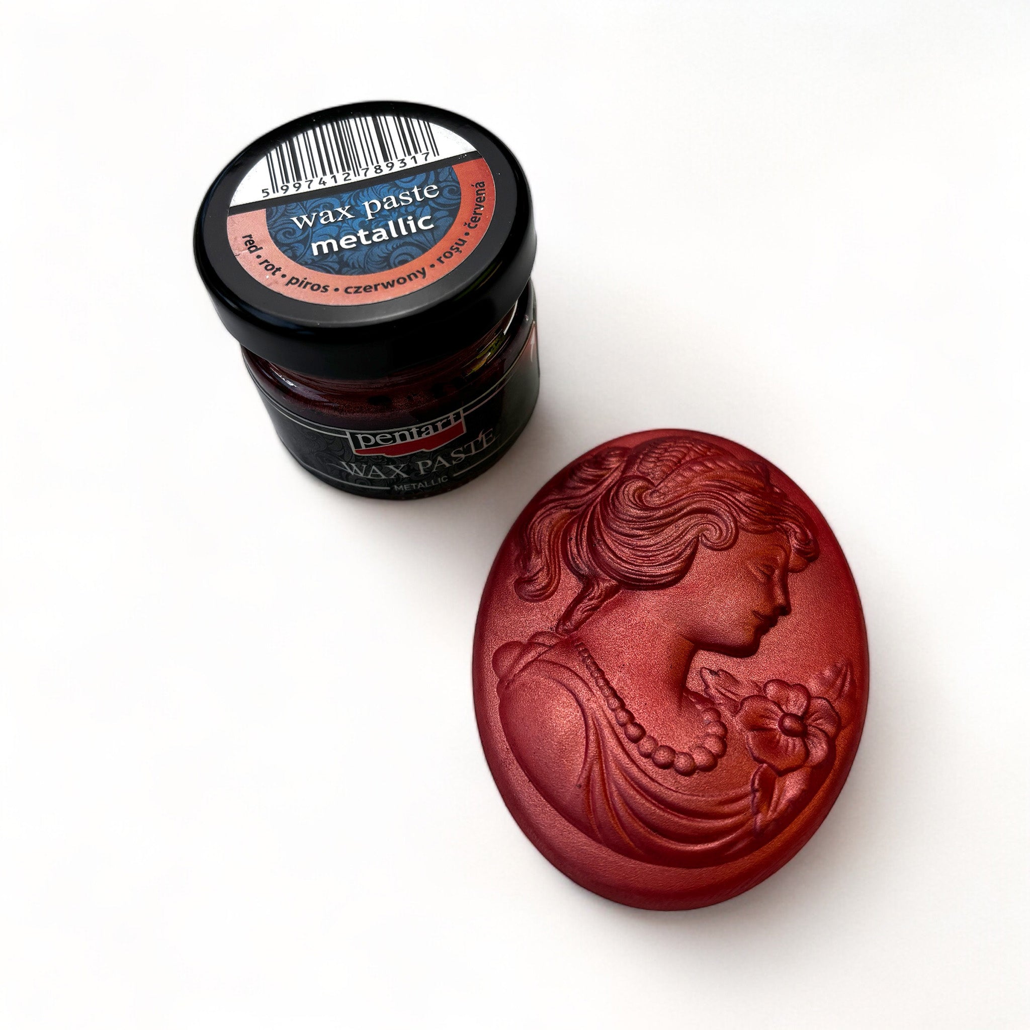 A jar of Pentart's Red Metallic Wax Paste and a silicone mold casting of a cameo pendant finished in the wax are against a white background.