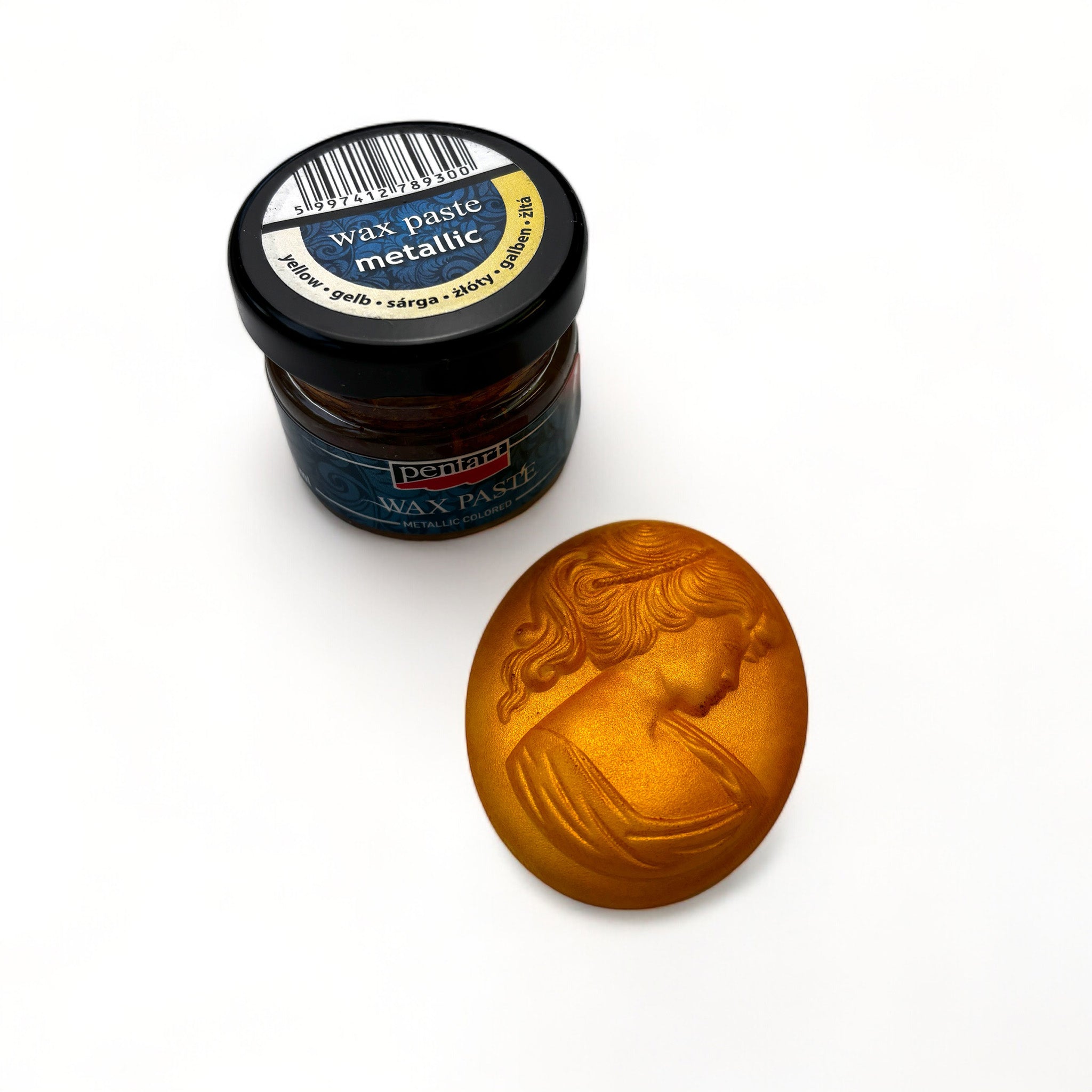 A jar of Pentart's Yellow Metallic Wax Paste and a silicone mold casting of a cameo pendant finished in the wax are against a white background.