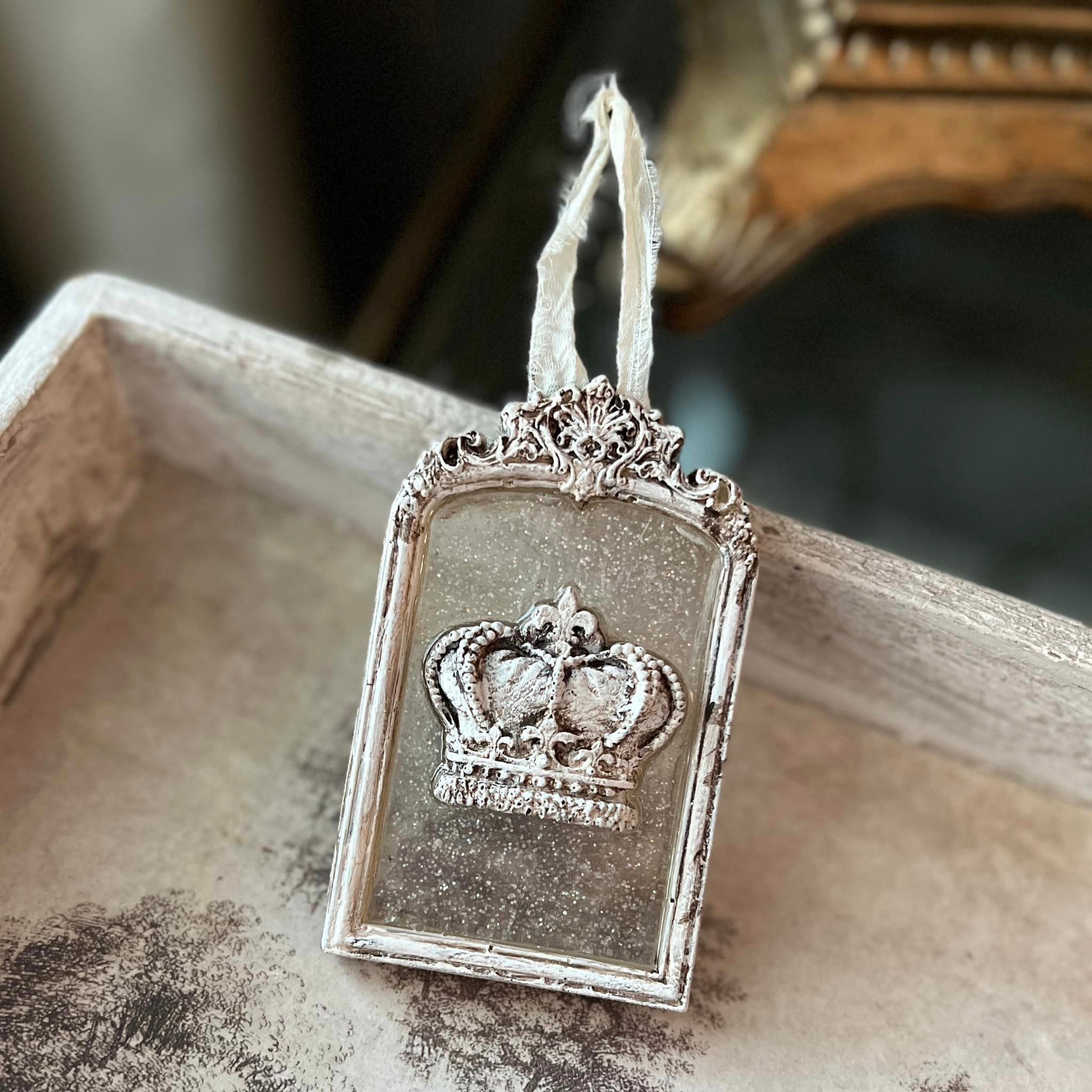 A small ornate silver colored frame featuring a clear resin center with a silver crown on it created from a silicone mold is propped up in a wood tray.