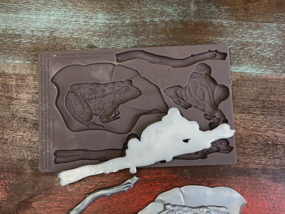 A 14 second video shows a close-up of ReDesign with Prima's Froggy Meadow Greens silicone mold and silver colored castings. A hand is shown picking up and holding the mold and a casting.