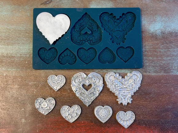 A 15 second video of Zuri Design's Valentine's Hearts silicone mold and silver colored castings are against a wood background. A hand is shown holding one of the large heart castings.