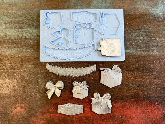 A 13 second video of LaBlanche's Christmas Gifts silicone mold and silver colored castings are against a wood background. A hand is shown holding one of the gift box castings.