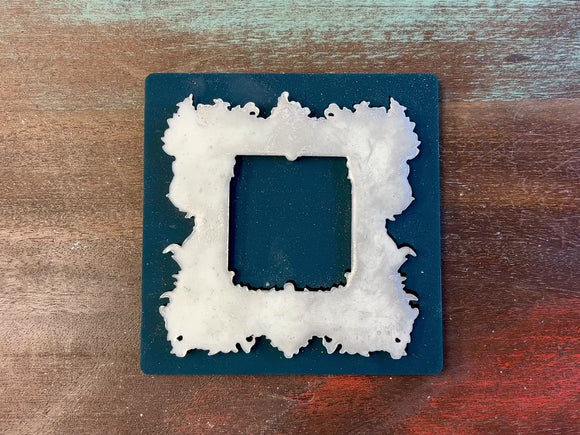 A video of Zuri Design's Square Frame silicone mold and silver colored casting are against a white background. A hand is shown holding the casting.