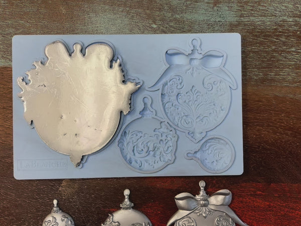 A 14 second video shows a hand lifting LaBlanche's Christmas Balls silicone mold and silver colored castings.