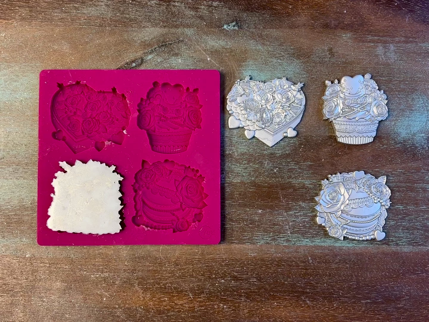 A 13 second video of Zuri Design's Valentine's Sweets silicone mold and silver colored castings are against a wood background. A hand is shown holding one of the castings.