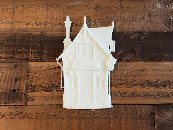 A 13 second video shows a close-up and backside of a white resin casting of a fairy house against a wood background. A hand is shown picking up the casting and turning it over.