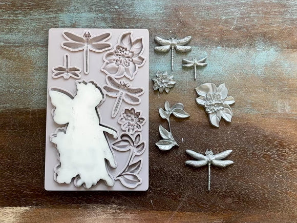 A 15 second video shows a close-up of Decoupage Queen's Garden Fairy silicone mold and silver colored castings against a wood background. A hand is shown picking up the fairy casting off of the mold.