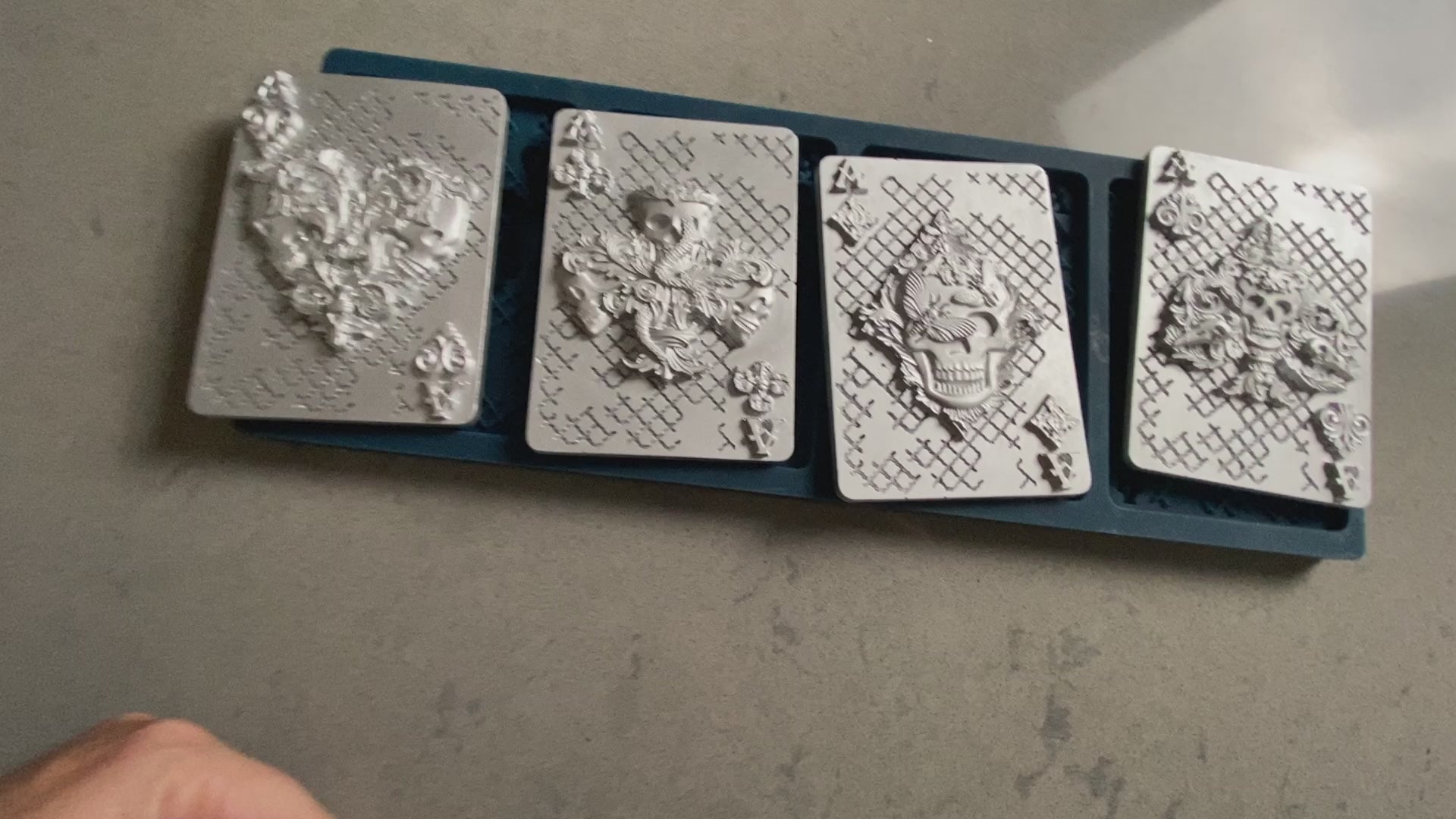 A 13 second video shows a close-up of Zuri Design's Aces of Darkness silicone mold and silver colored castings. A hand is shown picking up some of the castings.