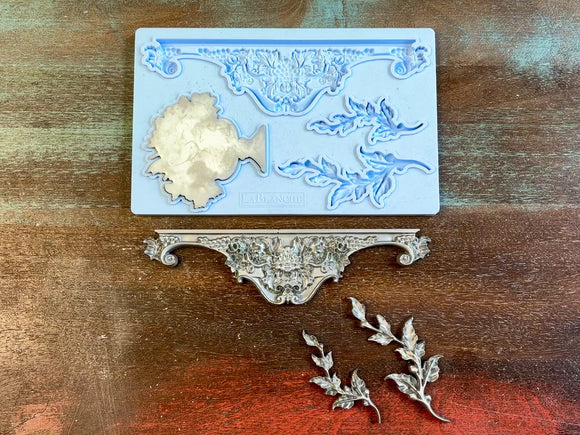 A 15 second video of LaBlanche's Ornament Louise silicone mold and silver colored castings are against a wood background. A hand is shown holding one of the castings.