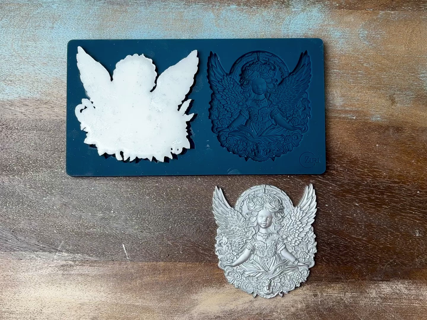 An 11 second video shows a close-up of Zuri Design's Cherub Twins silicone mold and silver colored castings against a dark wood background. A hand is shown picking up and holding one of the castings.