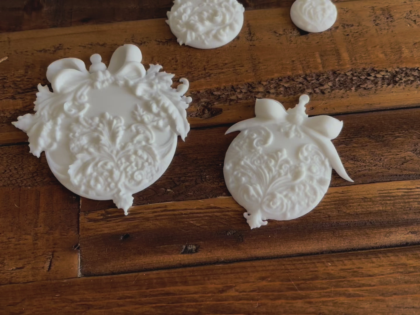 A 14 second video shows a close-up and backside of 4 white resin castings of ornate Christmas ornament baubles against a wood background. A hand is shown picking up one of the castings.