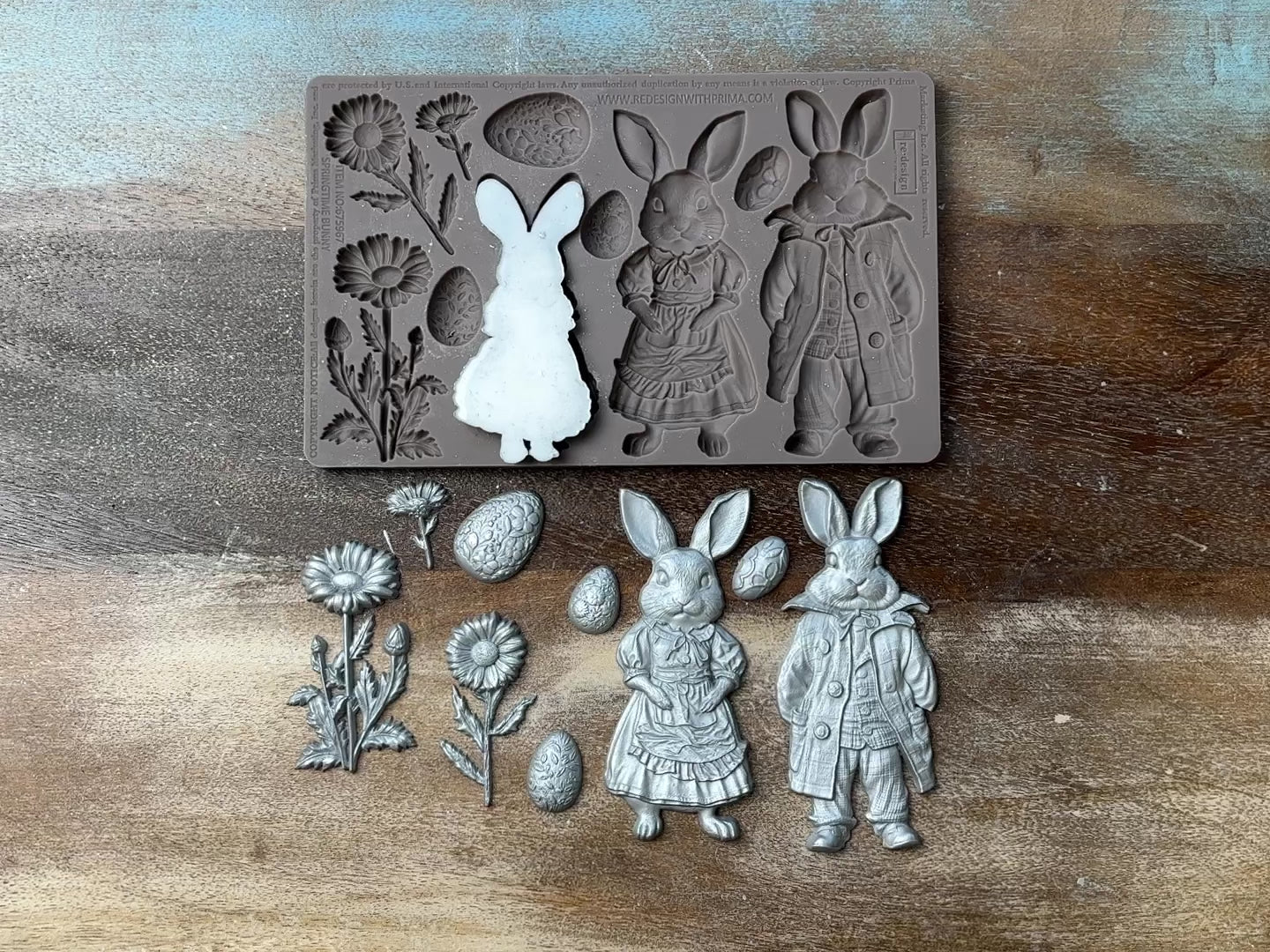 A 13 second video shows a close-up of ReDesign with Prima's Springtime Bunny silicone mold and silver colored castings against a wood background. A hand is shown picking up and holding one of the bunny castings.