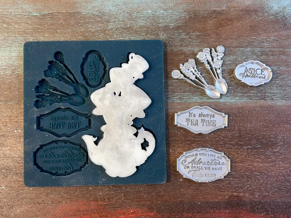 An 11 second video of Zuri Design's Tea Time silicone mold and silver colored castings are against a wood background. A hand is shown holding the teacups on a teapot casting.