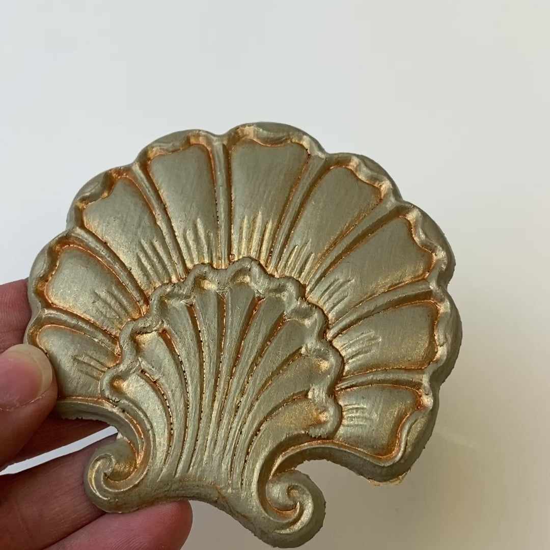 A 7 second video is shown holding a gold shell shaped flower silicone mold casting that has been detailed with Dixie Belle's Copper Glaze.