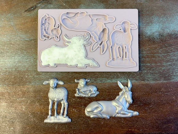 A 15 second video shows a close-up Decoupage Queen's Nativity Animals silicone mold and silver colored castings against a wood background. A hand is shown holding the ox casting. 