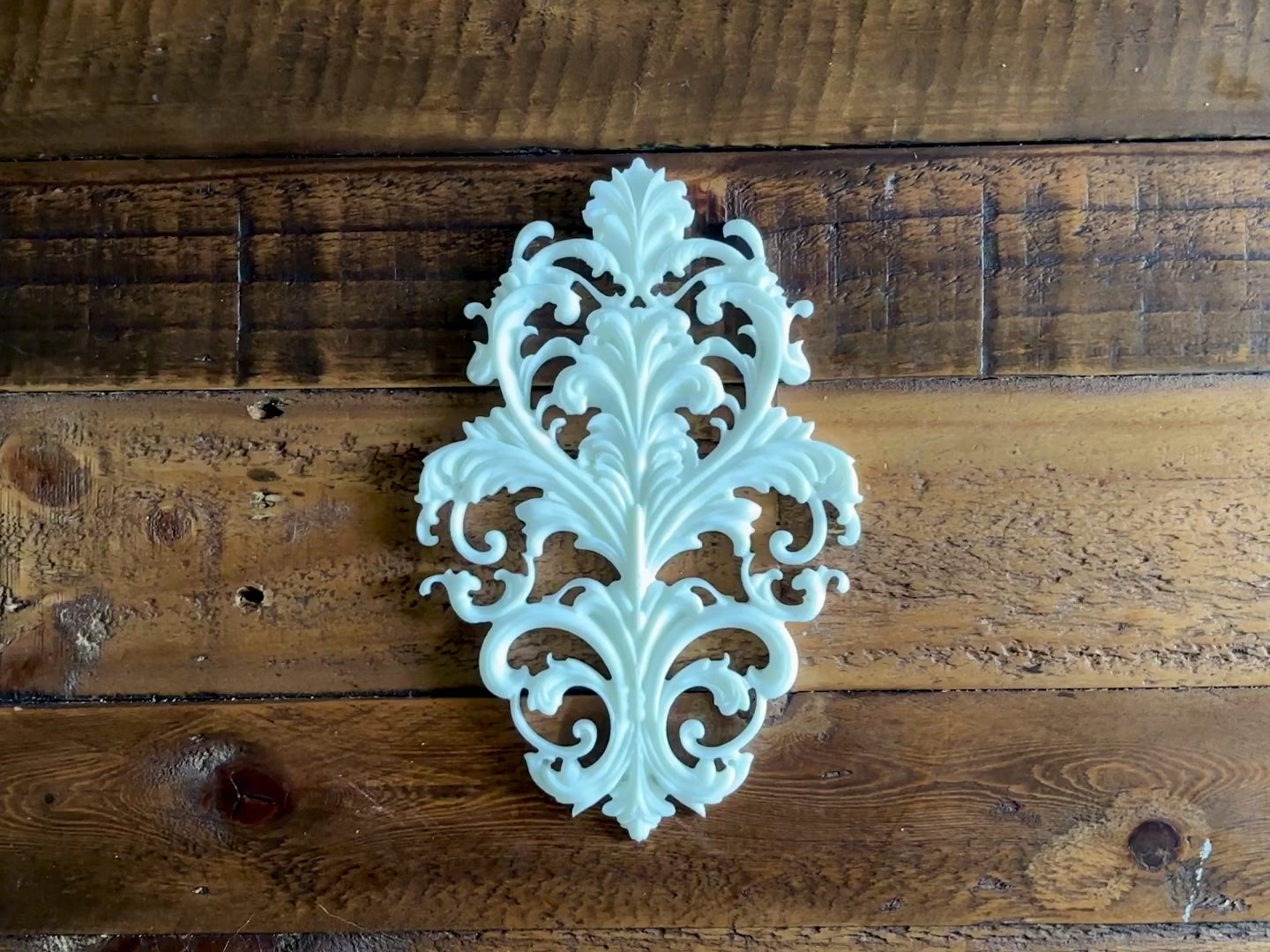 An 11 second video shows a close-up of a white resin casting created from LaBlanche's Baroque Emblem silicone mold against a dark wood background. A hand is shown picking up the casting.