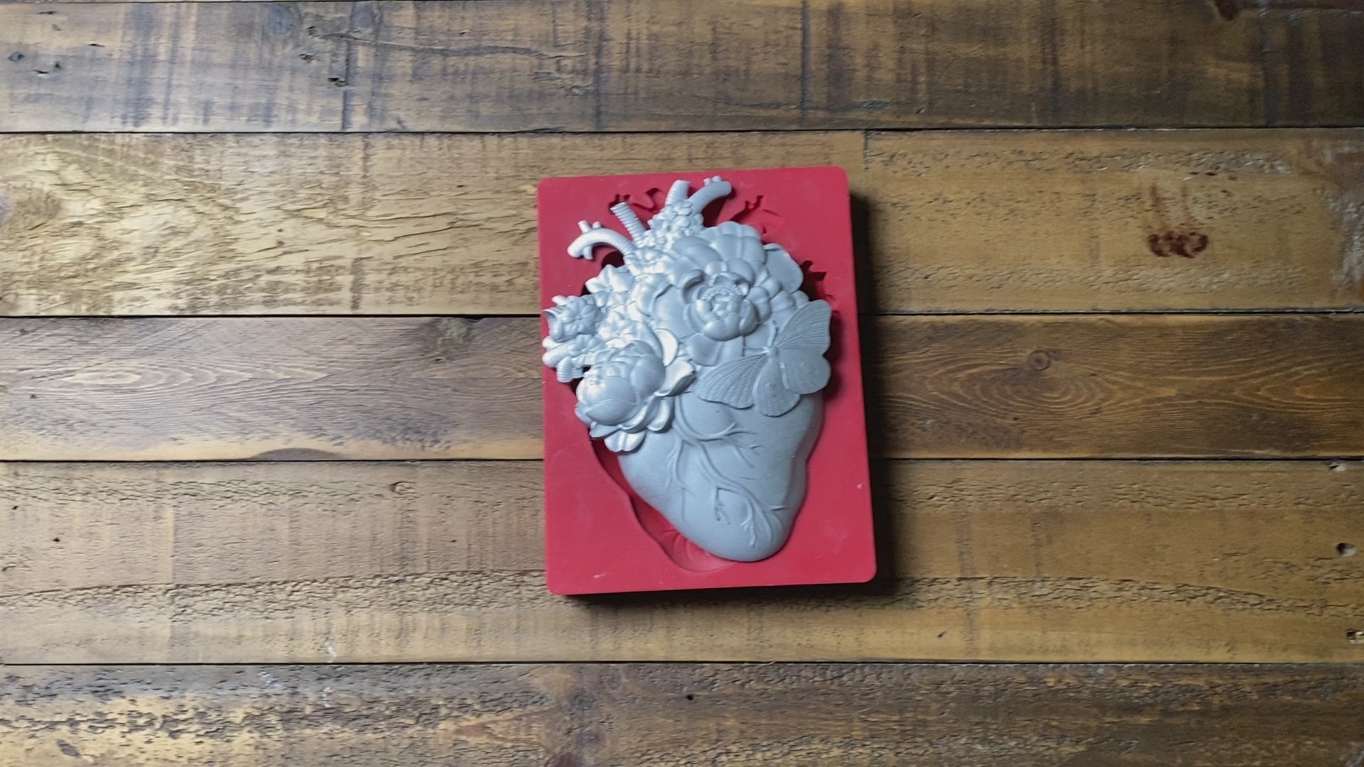 A 14 second videos shows a close-up of Get Inspired by Dadarkar Art's Blooming Heart silicone mold and silver colored casting against a dark wood background. A hand is shown picking up and holding the casting.