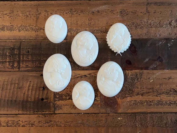 A 14 second video shows a close-up of 6 white resin cameo pendant castings created from LaBlanche's Vintage Cameo silicone mold against a wood background. A hand is shown picking up 1 of the castings.