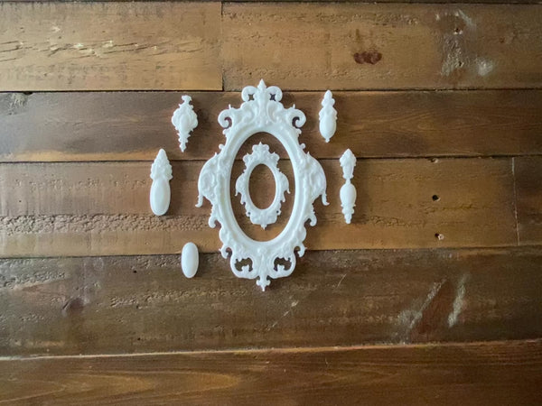A 13 second video shows a hand picking up white resin castings of 2 small ornate oval frames made from LaBlanche's Easter Baroque Frames silicone mould against a wood background.