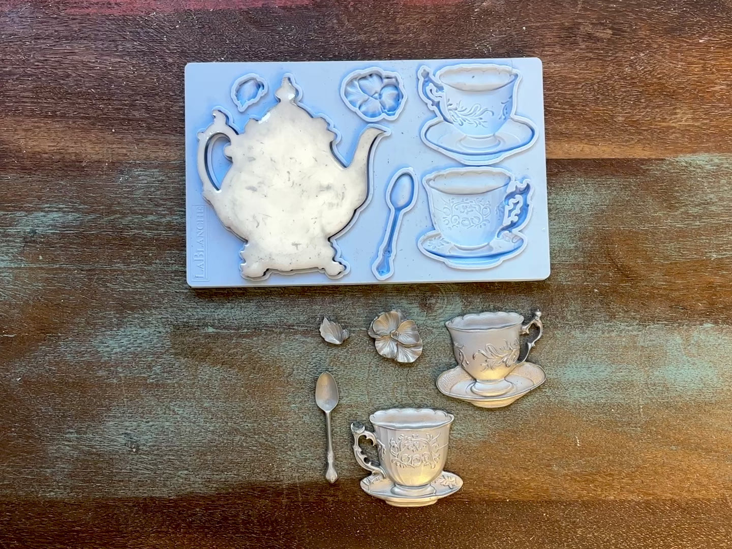 A 13 second video shows a close-up of LaBlanche's Tea Set silicone mold and silver colored castings against a wood background. A hand is shown picking up the teapot casting.