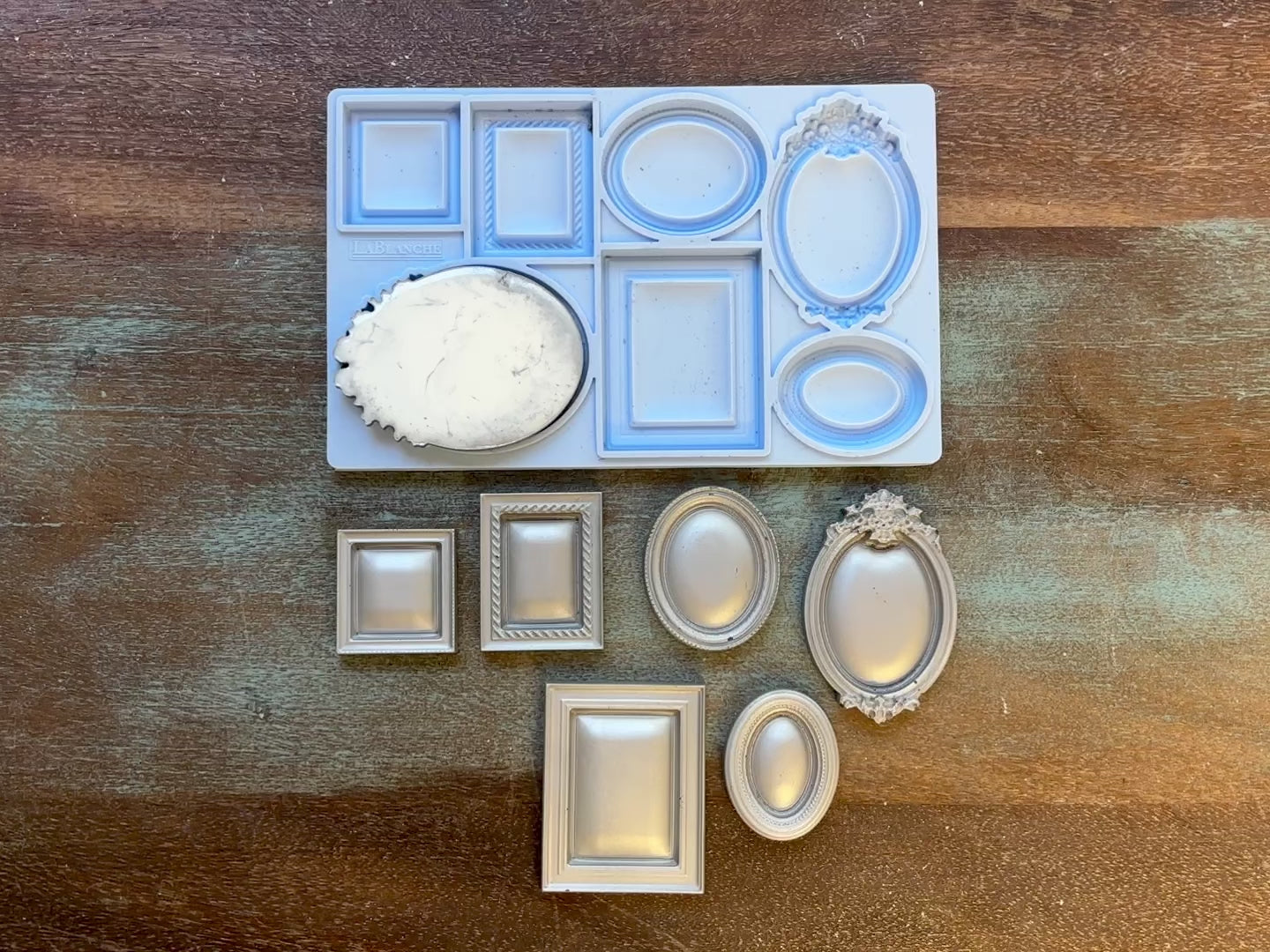 A 14 second video show a close-up of LaBlanche's Small Frames silicone mold and silver colored castings against a wood background. A hand is shown picking up one of the castings.