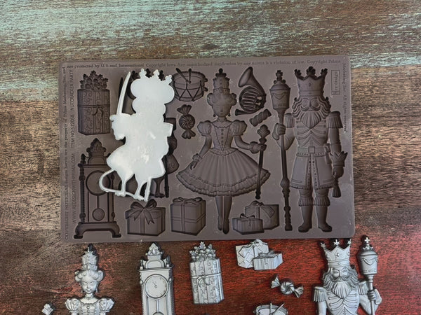 A 14 second video shows silver colored castings of ReDesign with Prima's Nutcracker Party silicone mold against a dark wood background and a hold picking up and holding the Mouse King casting.