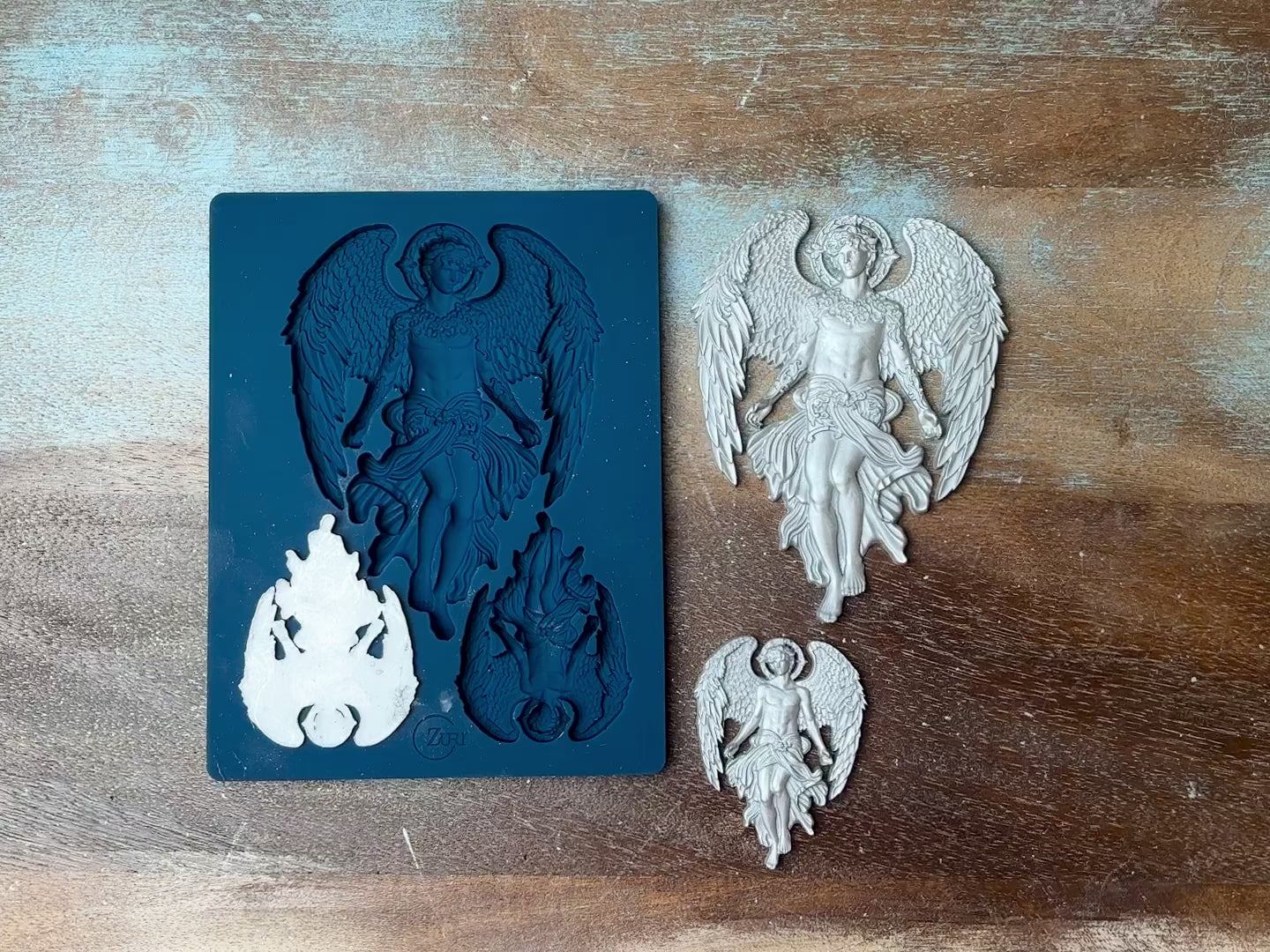 A 12 second video shows a close-up of Zuri Design's Celestial Guardian silicone mold and silver colored castings against a dark wood background. A hand is shown picking up one of the smaller castings.