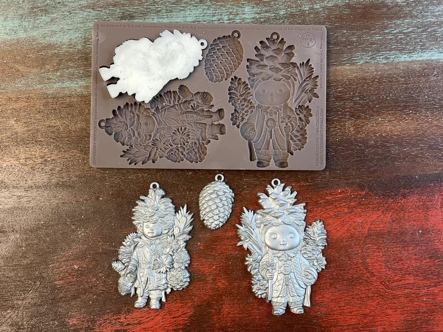 A 14 second video shows a close-up ReDesign with Prima's Pinecone Dolls silicone mold and silver colored castings. A hand is shown holding one of the castings.