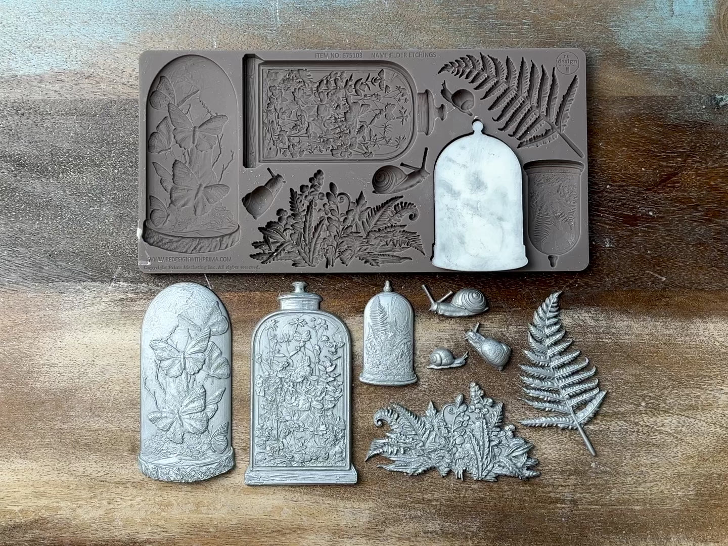 A 14 second video shows a close-up of ReDesign with Prima's Elder Etchings silicone mold and silver colored castings against a wood background. A hand is shown picking up and holding one of the castings.