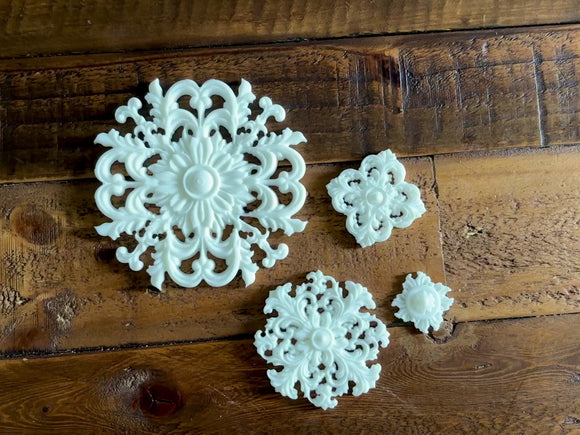 A 13 second video shows a close-up of 4 varying size white resin castings of round ornate medallions against a dark wood background. A hand is shown picking up and holding the largest casting.