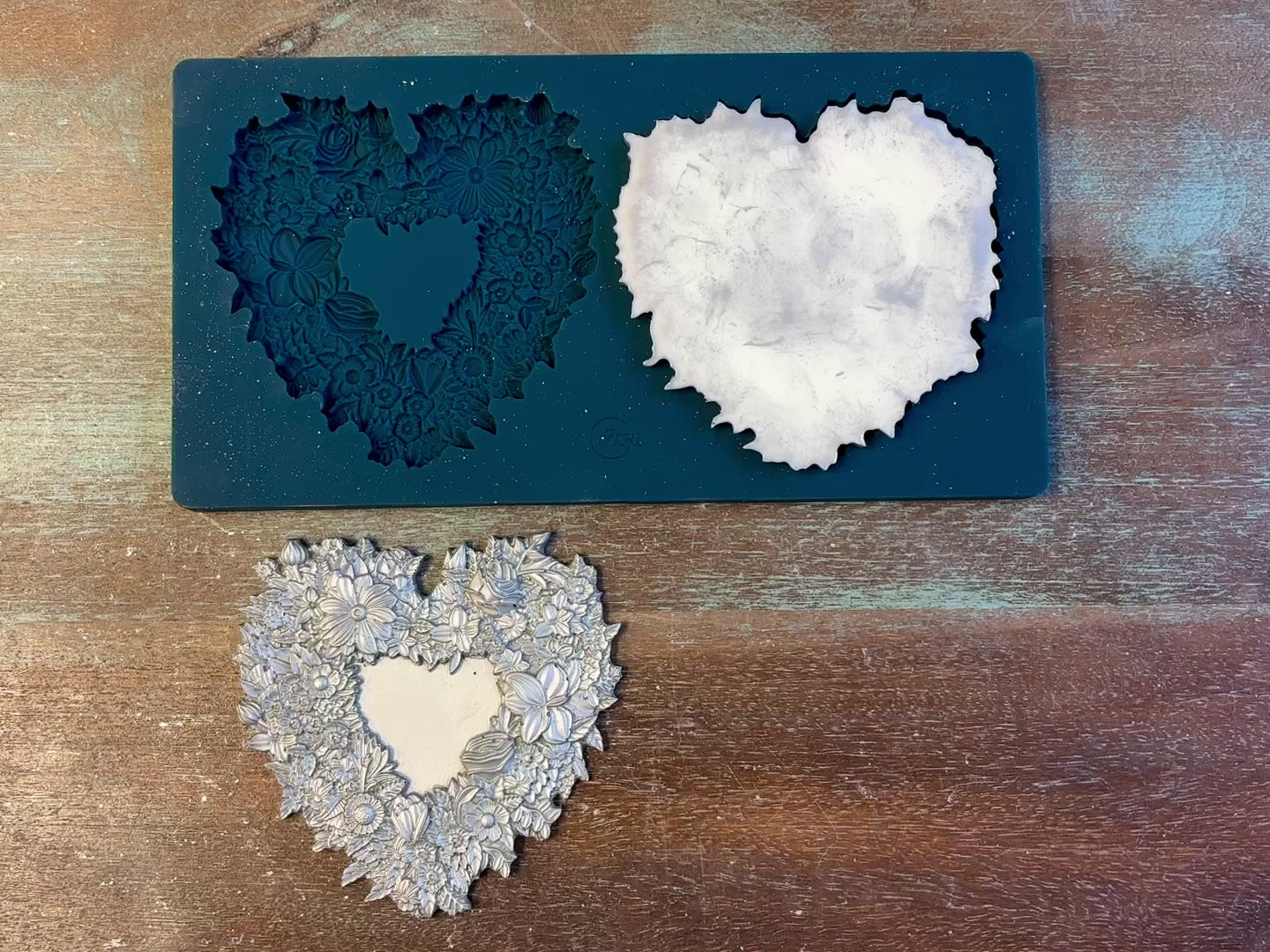 A 12 second video of Zuri Design's Floral Lovehearts Set 1 silicone mold and silver colored castings are against a wood background. A hand is shown holding one of the castings.