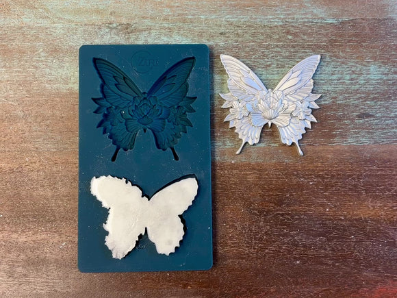 A 13 second video of Zuri Design's Butterfly Dance silicone mold and silver colored castings are against a wood background. A hand is shown holding one of the butterfly castings.