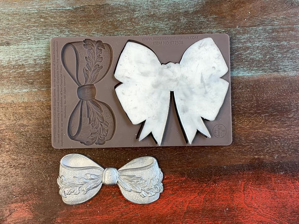 A 12 second video shows a close-up ReDesign with Prima's Vintage Opulence Bow silicone mold and silver colored castings. A hand is shown holding one of the castings.