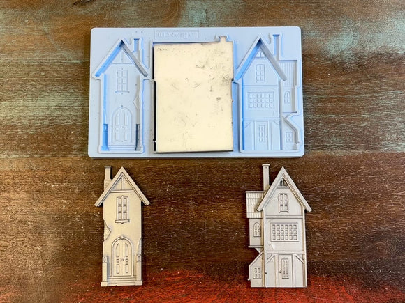 A 14 second video of LaBlanche's Houses 1 silicone mold and silver colored castings are against a wood background. A hand is shown holding one of the house castings.