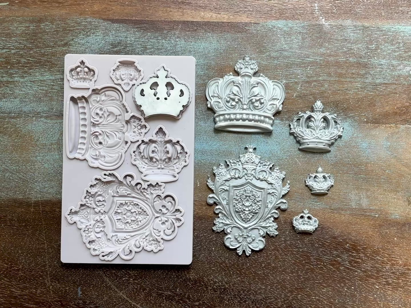 A 15 second video shows a close-up of Decoupage Queen's Regal Crowns silicone mold and silver colored castings against a wood background. A hand is shown picking up one of the crown castings off of the mold.