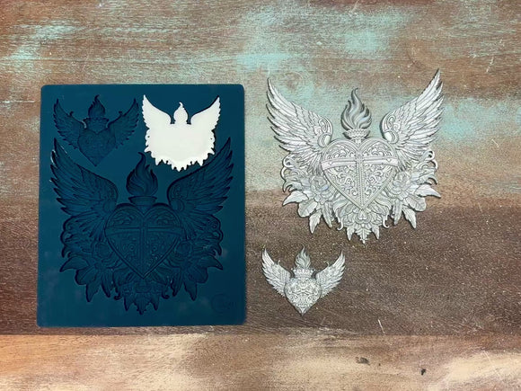 A 14  second video shows a close-up of Zuri's Sacred Hearts silicone mold and silver colored castings against a wood background. A hand is shown picking up on of the small heart castings.