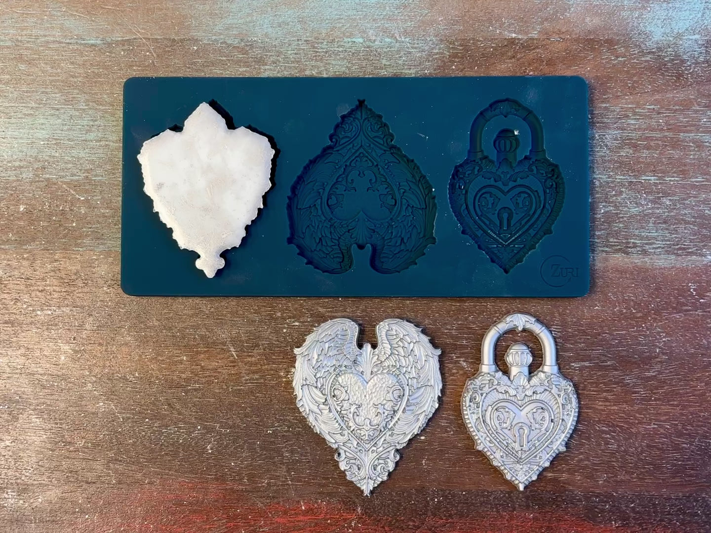 A 14 second video of Zuri Design's Gothic Hearts silicone mold and silver colored castings are against a wood background. A hand is shown holding one of the castings.