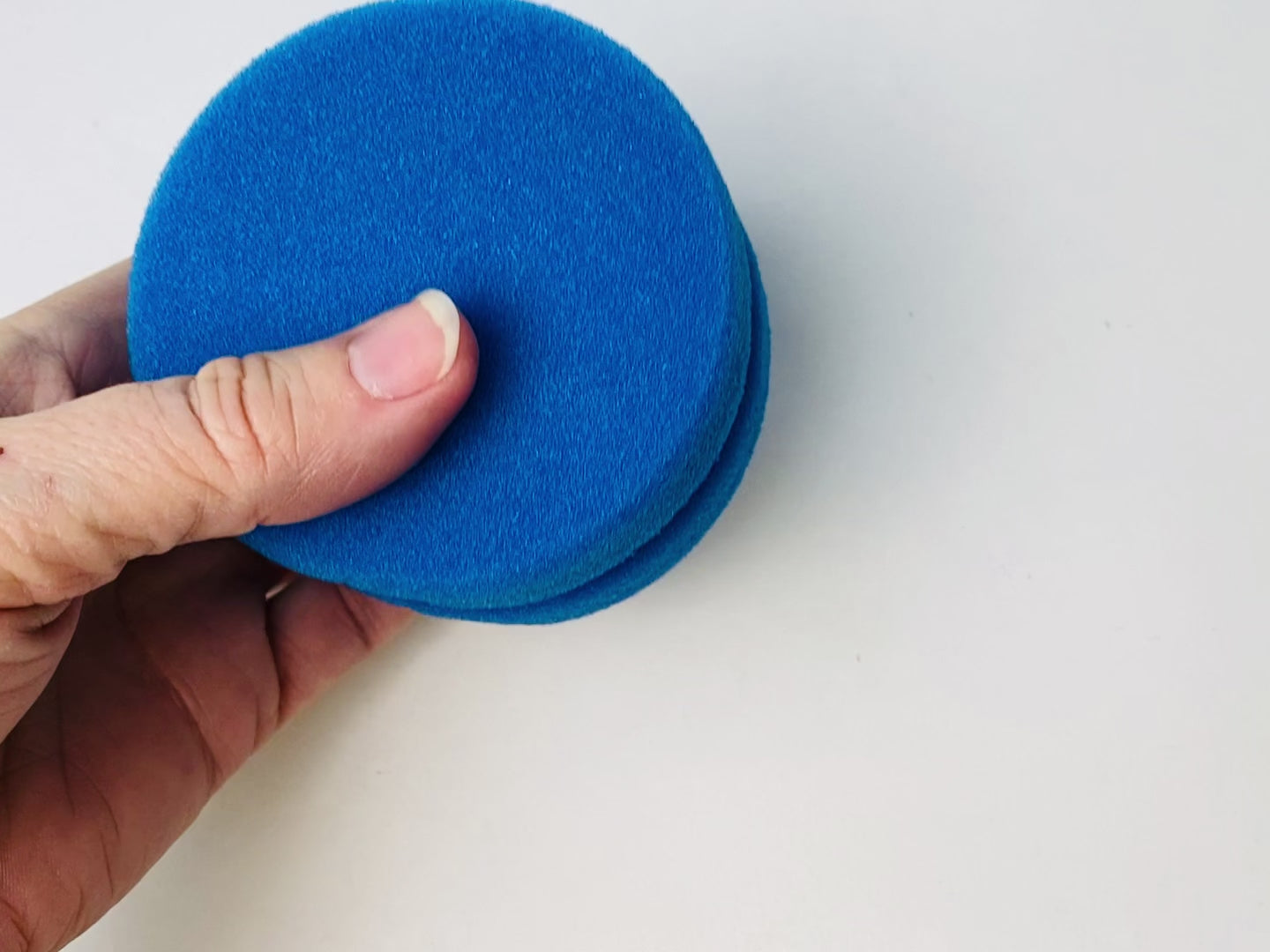 A 10 second video shows a hand holding, squeezing and turning Dixie Belle Paint's Blue Sponge Applicator against a white background.