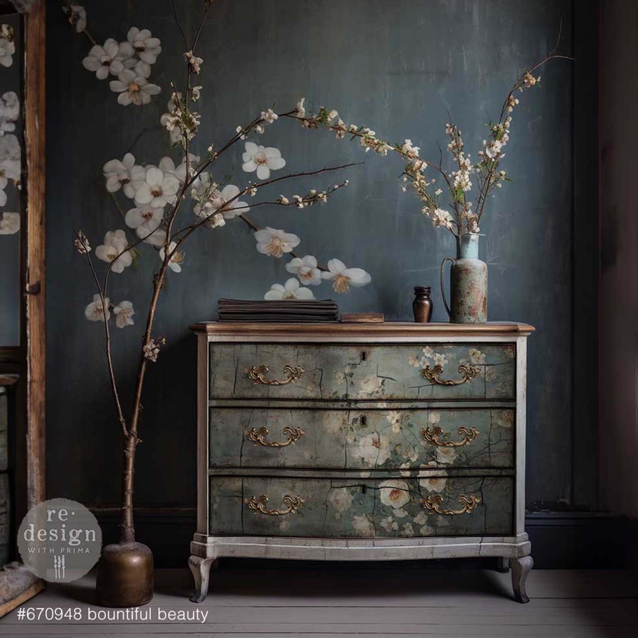 A vintage 3-drawer dresser is painted light gray and features ReDesign with Prima's Bountiful Beauty tissue paper of white roses on a faded blue background on its drawers.