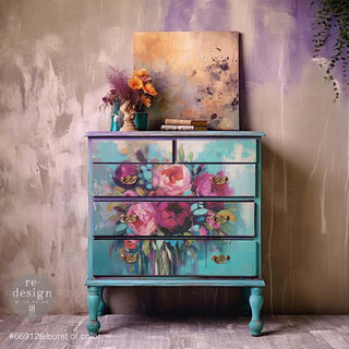 A vintage dresser is painted a blend of light teal-blue and purple and features ReDesign with Prima's Burst of Color A1 fiber paper on its 5 drawers.