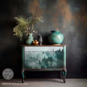 A vintage small dresser is painted a blend of mint green and dark brown and features ReDesign with Prima's Pine Grove Hue A1 fiber paper on its 3 drawers.