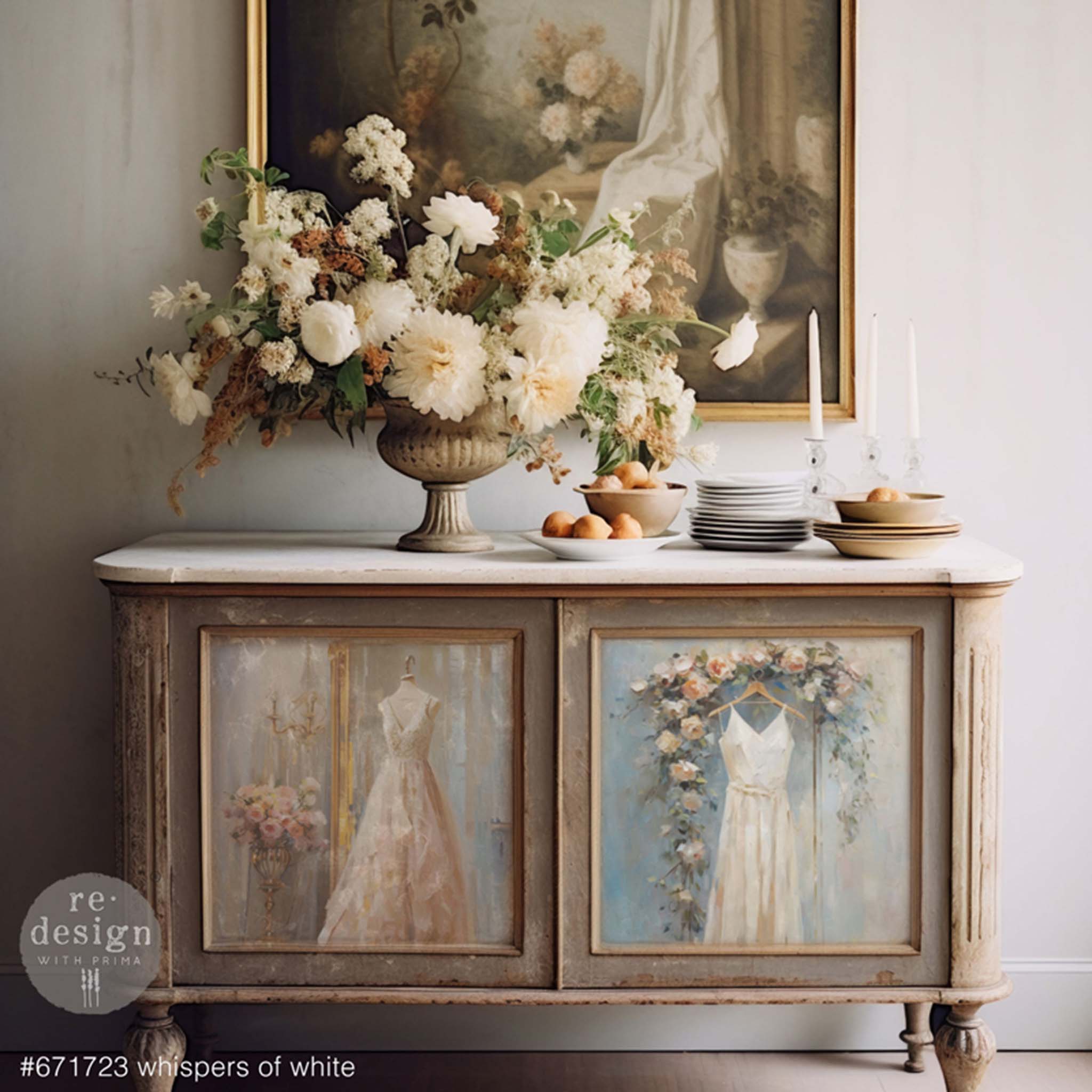 A vintage console table is painted beige and features ReDesign with Prima's Whispers of White tissue paper on its 2 doors. A large bouquet of flowers and dinnerware sit on the table.