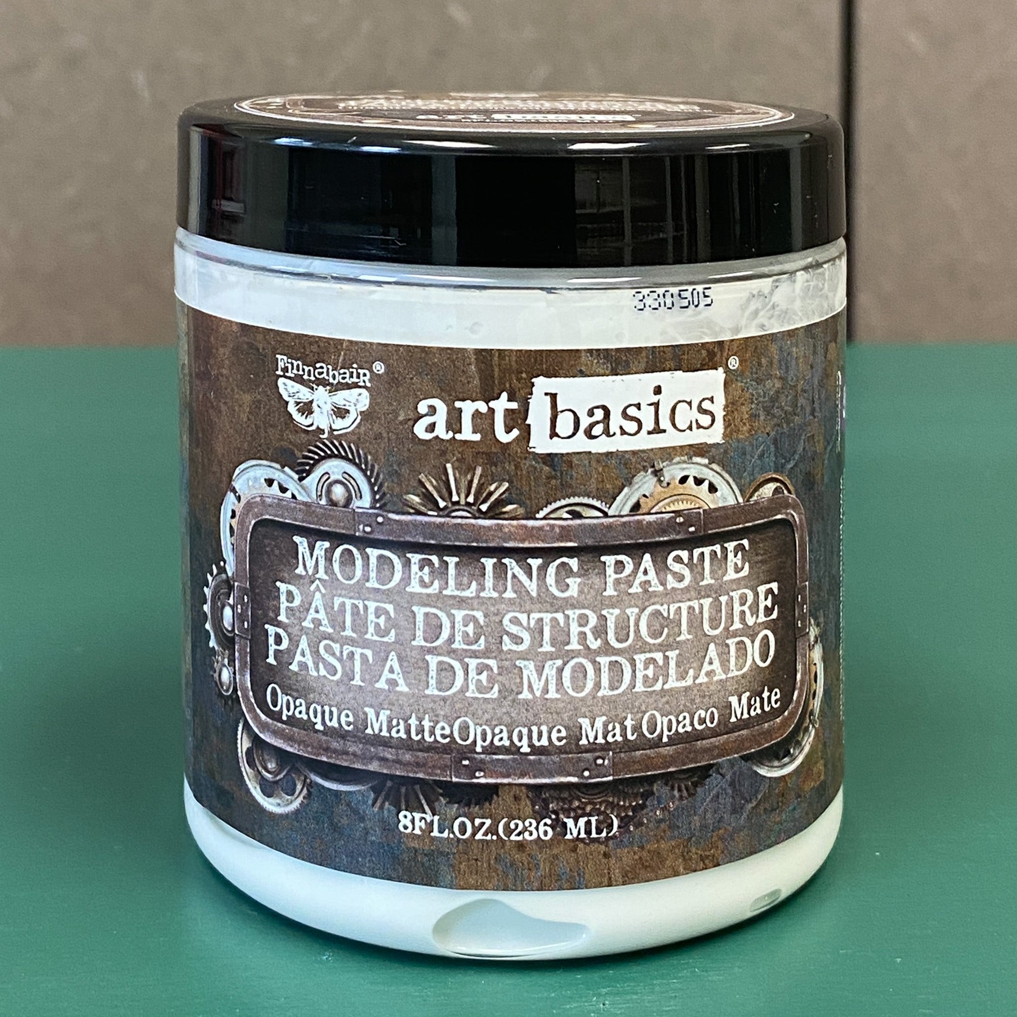 An 8 oz (236 mL) container of Finnabair's Art Basics Opaque Matte White Modeling Paste is against a light grey and teal background.