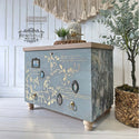 A modern 3-drawer dresser refurbished by Renovelle by Vilma, a ReDesign Brand Ambasador, is painted light blue and features A Bird Song on its drawers.
