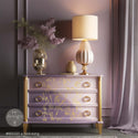 A 3-drawer dresser refurbished by ReDesign with Prima is painted light purple and cream with gold accents and features A Bird Song on its drawers.