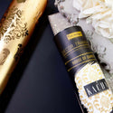 The tube and gold foil roll of House of Damask is on a black surface.