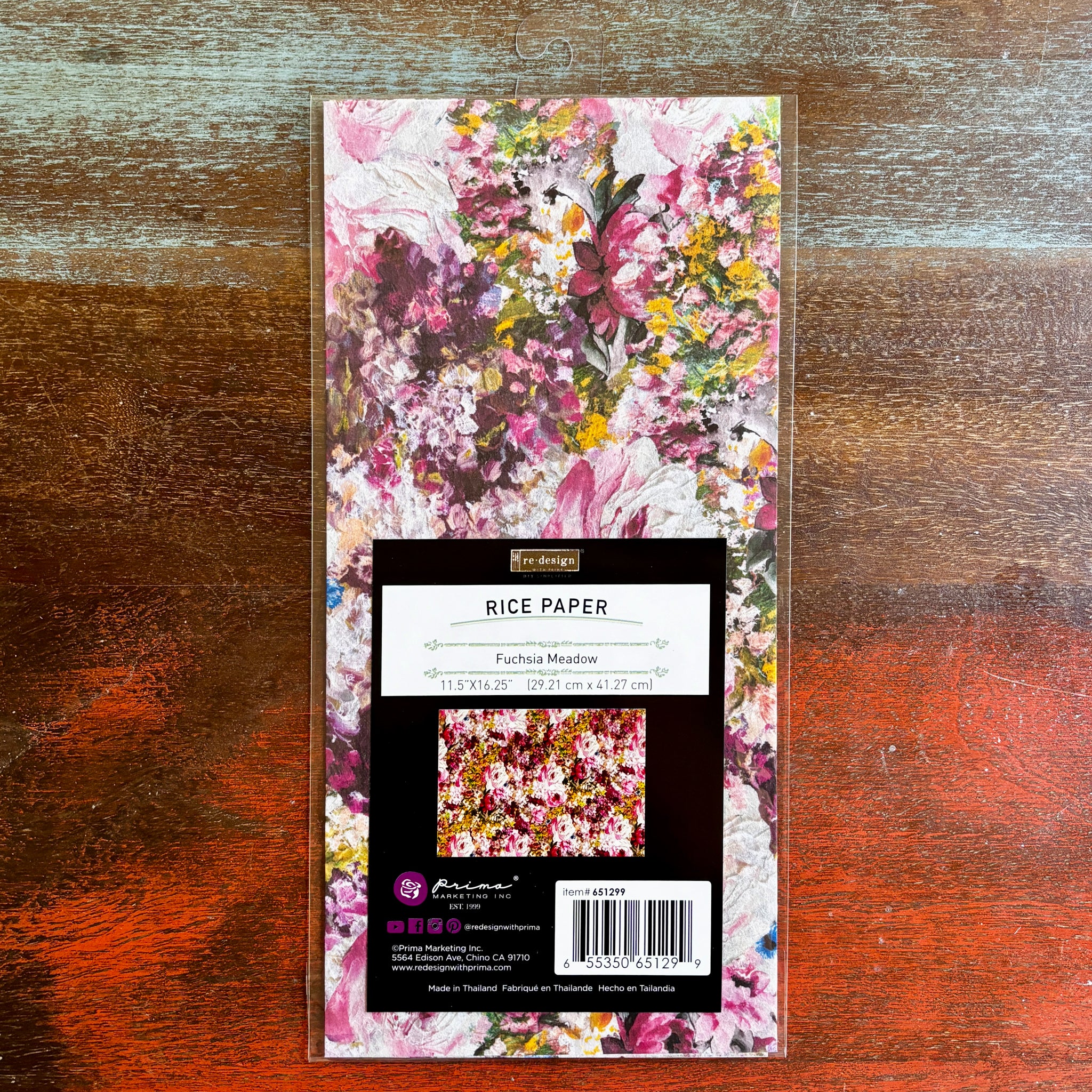 A package of ReDesign with Prima's Fuchsia Meadow rice paper is against a dark wood background.