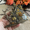 Halloween-themed miniature house with pumpkins and a ghost on a hand, with autumn leaves in the background.